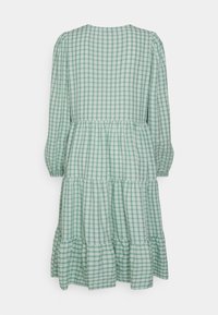 Vestido verde e branco xadrez com mangas longas, babados em camadas na barra e decote arredondado. Feito de um tecido leve.