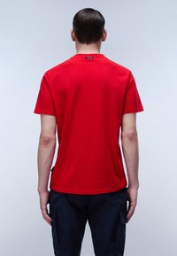 Rød bomulds T-shirt med rund halsudskæring og korte ærmer, med minimal syning og et lille mærke på bagsiden.