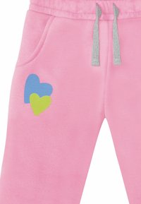 Lyserøde sweatpants med snøre i livet, med et blågrønt hjerte-design på venstre ben og sidelommer.
