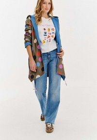 Niebieska kurtka z kapturem w duże, wielokolorowe kropeczki, biała koszulka z grafiką, jasnoniebieskie dżinsy i wzorzyste trampki.