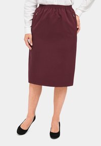 Bordeauxlange broekrok met een elastische tailleband, voorzien van zijzakken en een gladde textuur. Gepaard met zwarte Suède pumps.