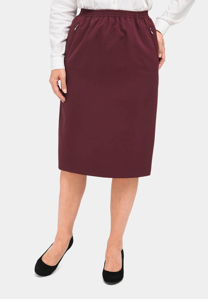 Bordeauxlange broekrok met een elastische tailleband, voorzien van zijzakken en een gladde textuur. Gepaard met zwarte Suède pumps.
