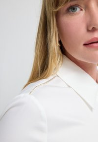 Witte blouse met een puntkraag, voorzien van een metallic ritssluiting op de schouder en een zachte, gladde stofstructuur.