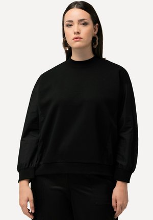 Sweatshirt noir avec un col montant et des manches longues légèrement bouffantes. Le tissu semble doux et légèrement texturé, avec une coupe décontractée.