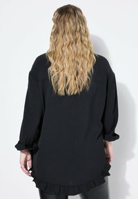 Camisa negra de manga larga, fabricada en tejido ligero, con un corte relajado, cuenta con un dobladillo con volantes, puños abotonados y un diseño de espalda redondeada.