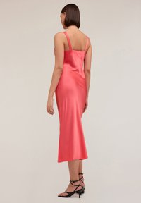 Rochie din satin roz, cu bretele subțiri, lungime până la jumătatea gambei, și o textură netedă, asortată cu sandale cu toc, cu curele negre.