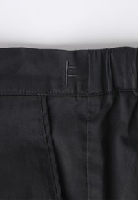 Ceinture en tissu noir avec un détail de couture subtil et un logo. Texture douce et lisse avec une section élastique froncée pour le confort.