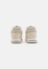 Sneaker beige con retro testurizzati, dotati di una parte superiore in pelle liscia, suola bianca e accenti grigi. Design semplice, dettagli di branding minimi.