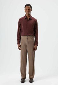 Chemise bordeaux à manches longues avec boutons, associée à un pantalon beige à fines rayures, présentant une texture douce et une coupe classique. Des chaussures marron complètent le look.