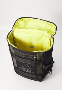 Černý sportovní batoh s žlutým interiérem, síťovými kapsami a zipovými uzávěry; obsahuje kontrastní prošívání a logo Adidas na přední straně.