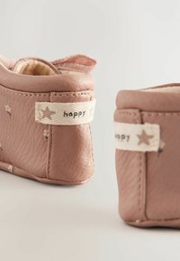 Weiche rosa Lederbabyschuhe mit Blumenmustern, plüschigem Futter und einem Stoffetikett mit dem Wort "happy" und Sternakzenten an der Seite.