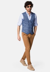 Niebieska kamizelka w kratę na jasnoniebieskiej koszuli, połączona z brązowymi spodniami i beżowymi trampkami. Uzupełniona o ciemne okulary przeciwsłoneczne.