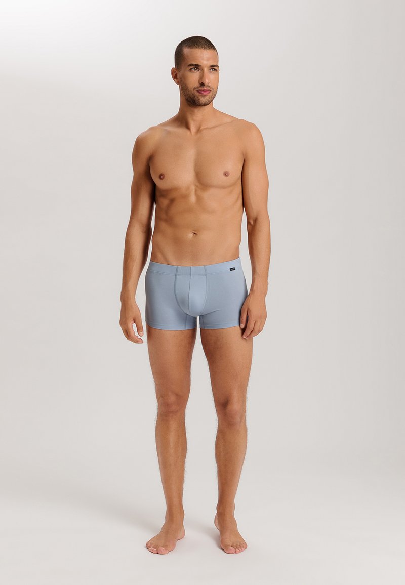 Ljusblå herrboxershorts gjorda av mjukt tyg, med en figurnära design och elastisk midja, som bärs av en modell utan tröja.