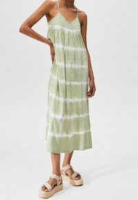 Robe maxi tie-dye vert clair avec bretelles spaghetti, taille froncée et tissu doux. Associée à des sandales plateforme beige.