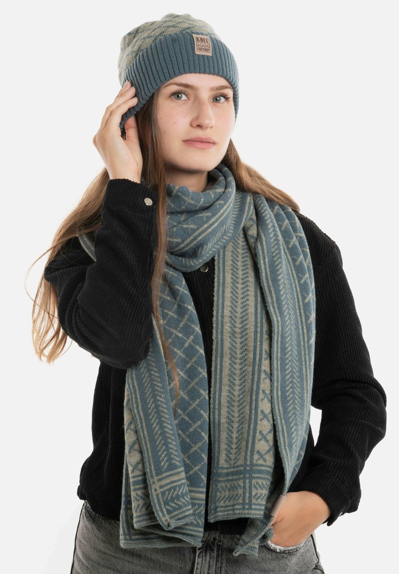 Gehaakte wollen muts in licht en donkerblauw met een gestructureerde band; gegooide sjaal in bijpassende tinten, met geometrische ontwerpen.
