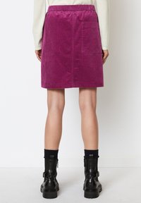 Jupe en velours côtelé violet avec une taille élastique et une poche arrière, présentant une coupe droite qui tombe au-dessus du genou, associée à des bottes noires.