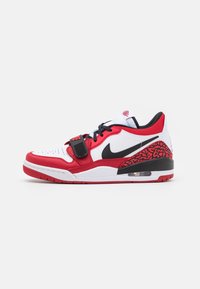 Zapatilla atlética roja y blanca con acentos negros, que presenta un panel texturizado rojo con patrones, una correa sobre los cordones y amortiguación de aire visible.