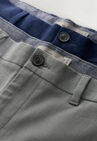 Deux pantalons pliés, un gris et un bleu marine, avec des boutons visibles et des passants de ceinture sur une surface claire.