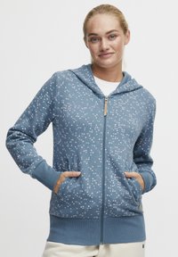 Blå zip-up hoodie med ett spräckligt mönster i rosa och vitt, med en dragsko i huvan och framfickor. Ribbad muddar och nederkant.