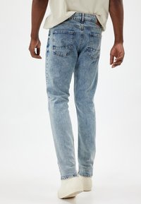 Jeans in denim azzurro chiaro con taglio dritto, dotati di due tasche posteriori, leggere pieghe e dettagli di cucitura standard.
