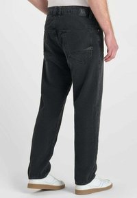 Jean en denim noir avec un design à jambes droites, comportant des poches arrières et une finition texturée. Porté avec des baskets blanches et un haut léger.