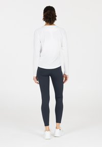 Vit långärmad topp med rund hals, kombinerad med mörkblå leggings och vita sneakers. Toppens material är slätt och lätt.