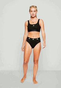 Juodas sportinis trumpintis topas ir kelnaitės su aukštu liemeniu. Turintis logotipo akcentus ant liemenėlės. Lygi medžiaga, minimalistiškas dizainas.