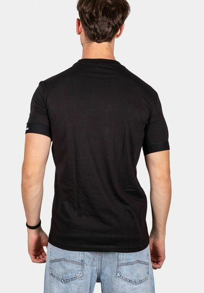 T-shirt di cotone nero a maniche corte, con un design semplice e un piccolo accento nero vicino alla manica. Il modello indossa jeans azzurri.