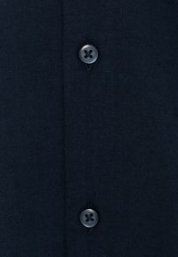 Tmavě modrá košile na knoflíky se dvěma černými knoflíky se čtyřmi dírkami, texturovanou tkaninou a čistým designem předního límce.