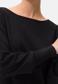 Schwarzes Langarmshirt mit weitem Boot-Ausschnitt. Hergestellt aus weichem Stoff, mit Raffungen an den Schultern und enganliegenden Ärmeln.