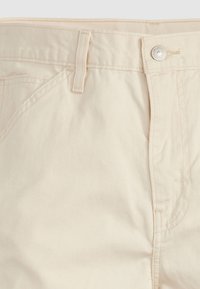 Pantalones de algodón beige con una cintura estándar, cremallera y bolsillos laterales, con costuras sutiles y una textura suave.