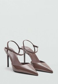 Tacchi slingback in vernice marrone con punta affusolata, tacco a stiletto e cinturino alla caviglia regolabile. Texture liscia con dettagli minimi.