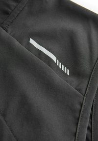 Gros plan d'un tissu noir avec une bande réfléchissante blanche composée d'une longue ligne et de six lignes parallèles plus courtes.