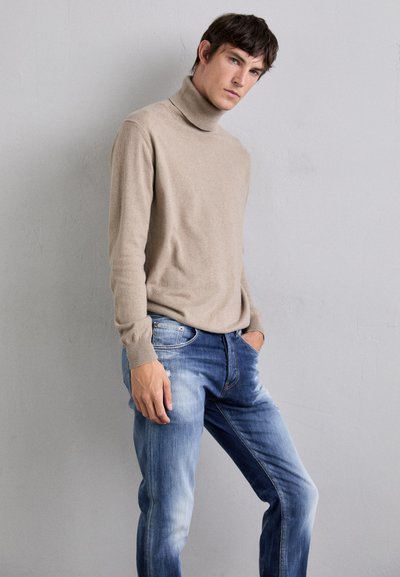 Maglione beige a collo alto in morbido tessuto a maglia abbinato a jeans in denim azzurro chiaro con finitura strappata e accenti sbiaditi.