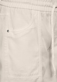 Pantalones cargo de color beige claro con una cintura elástica, cordón ajustable y un bolsillo frontal con un detalle de botón a presión plateado.