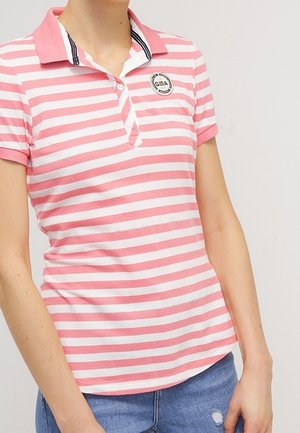 Vrouw draagt een roze-wit gestreept poloshirt met korte mouwen, een kraag en een klein rond logo op de borst, gecombineerd met een blauwe spijkerbroek.