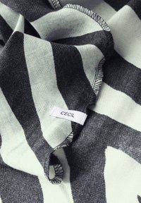 Vaaleansininen kangashuivi, jossa on tummanharmaita chevron-raitoja, ja jossa on valkoinen etiketti, jossa lukee "CECIL". Tekstuuri on pehmeä, ja siinä on näkyviä ompelusaumoja.