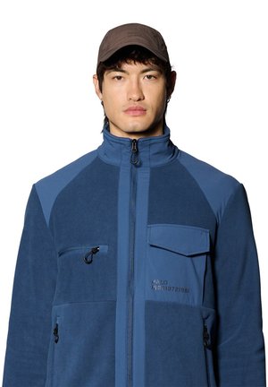 Blue fleece jacket with a high collar, zip closure, and a chest pocket. The design features contrasting fabric textures and color shades.