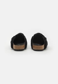 Črne puhaste natikače s plastičnim podplatom iz plute, ki imajo debel trak in zaobljen hrbet, poudarjajo mehko teksturo in minimalističen dizajn.