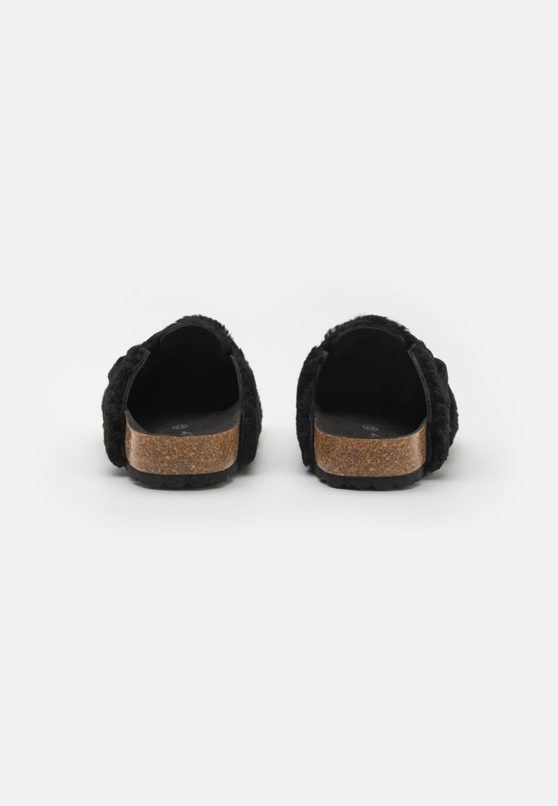 Schwarze, flauschige Clogs zum Hineinschlüpfen mit Korksohle, ausgestattet mit einem dicken Riemen und rundem Rücken, der die weiche Textur und das minimalistische Design betont.