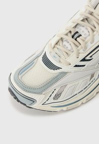 White and light blue athletic shoe with mesh upper, textured overlays, and lace-up design; features black accents and rubber sole.