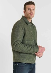 Chaqueta de lana verde con cierre de cremallera, diseño con cuello, bolsillos delanteros y un acabado texturizado. Corte clásico con mangas largas.