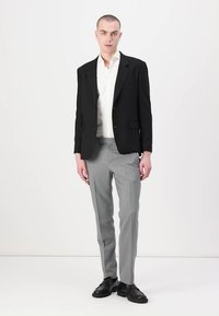 Schwarzes Sakko mit zwei Knöpfen, weißes Hemd und hellgraue Hose. Schwarze eleganten Schuhe, taillierte Passform, glatte Textur und klare Linien.