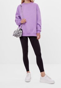 Felpa oversized lavanda, leggings neri, sneakers bianchi e una borsa a tracolla in stampa zebra bianca e nera con tracolla in argento.