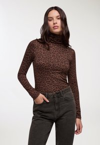 Maglia a collo alto a maniche lunghe con stampa leopardata marrone, dal design aderente, abbinata a jeans scuri a vita alta, con una leggera texture.