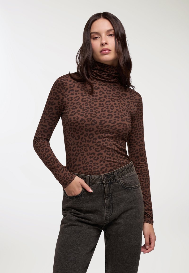 Maglia a collo alto a maniche lunghe con stampa leopardata marrone, dal design aderente, abbinata a jeans scuri a vita alta, con una leggera texture.