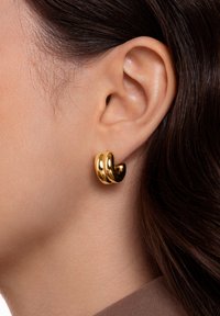 Orecchini color oro con una finitura liscia e lucida. Il design presenta tre bande intrecciate, creando un aspetto scultoreo.