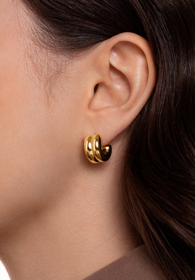 Orecchini color oro con una finitura liscia e lucida. Il design presenta tre bande intrecciate, creando un aspetto scultoreo.