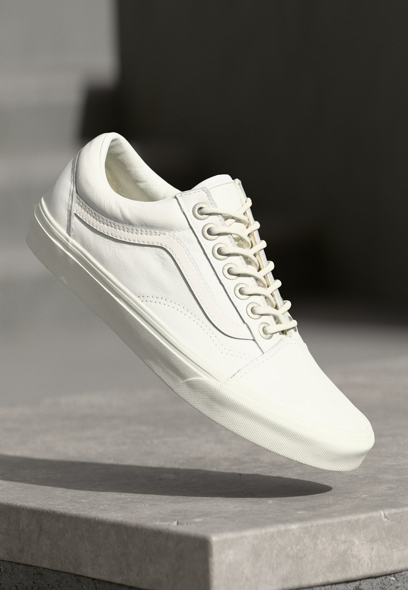 White leather sneaker with a smooth texture, round toe, and flat rubber sole. Features five eyelets and side stripe detail.