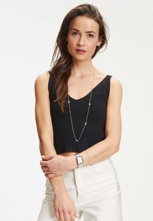 Zwart geribbeld crop top met een V-hals, gecombineerd met witte hooggewaisted jeans. Accessoires omvatten een lange zilveren ketting en een zilveren horloge.